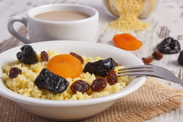 Cooked millet groats on white plate and cup of coffee with milk, healthy food and nutrition
