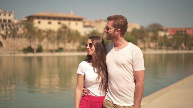 4k footage, young hugging couple walking along pond in front of cathedral during sightseeing tour
