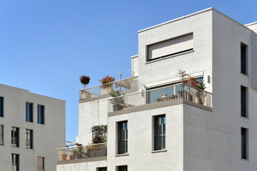 Fragment of white residential buildings with balconies,  plants and rectangular windows on a background of blue sky
