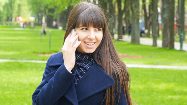 Young woman talking on the modile phone in a city park. Green ni