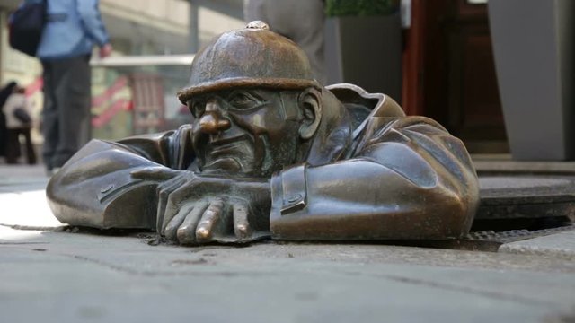 Cumil - statue of man peeking out from under a manhole cove
