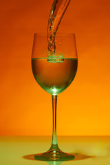 Green falling water flow into wineglass and creating a swirl.