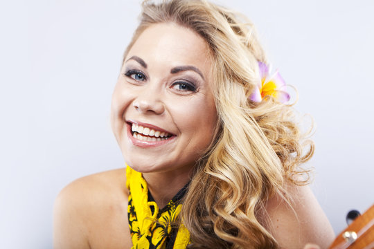 Cheerful young blonde in a Hawaiian scarf. Girl plays on ukulele. Hawaii style. Portrait of a smiling woman
