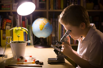 Close-up portrait of young student working with microscope in his room. Child and science experiments. Kid studying samples under the microscope. Preparing for science lesson.