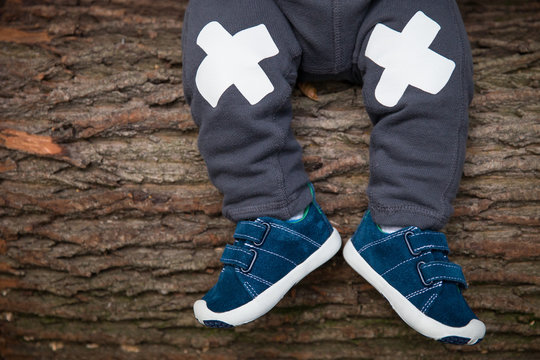 Close-up of baby's legs in sneakers on the wooden tree background. Little child sitting on old tree - image of legs and feet.