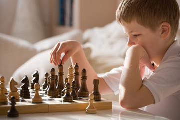 Boy playing chess in the room. Little clever boy concentrated and thinking while playing chess at...
