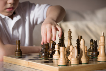 Boy playing chess in the room. Little clever boy concentrated and thinking while playing chess at home.