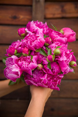 Beautiful bouquet of dark pink peonies in woman hands on a wooden background. Bunch of flowers in hands. Stripes. Summer time.