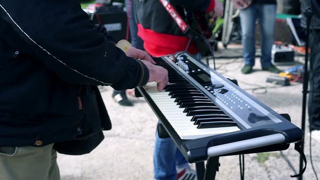 Closeup of keyboard player hands performing with band at outdoor concert
