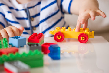 Close up of child's hands playing with colorful plastic bricks at the table. Toddler having fun and...