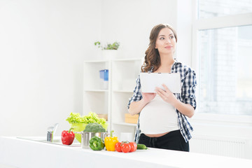 Beautiful pregnant woman in the kitchen surfing in tablet