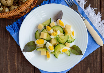 Light Italian Spring salad with fresh cucumber, quail eggs, mozzarella, olive oil on a white plate on a wooden background. Dietary meal.