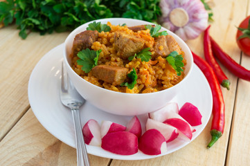 Traditional Asian sharp pilaf with fresh herbs, garlic, carrots and meat in a white bowl on a wooden background