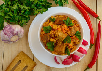 Traditional Asian sharp pilaf with fresh herbs, garlic, carrots and meat in a white bowl on a wooden background