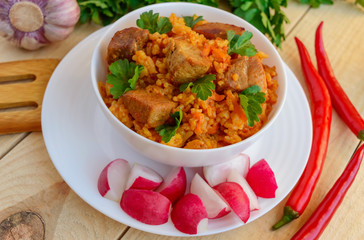 Traditional Asian sharp pilaf with fresh herbs, garlic, carrots and meat in a white bowl on a wooden background