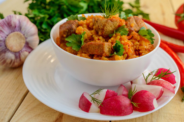Traditional Asian sharp pilaf with fresh herbs, garlic, carrots and meat in a white bowl on a wooden background