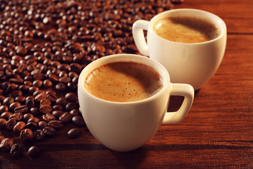 Two cups of fresh coffee with beans on table, closeup