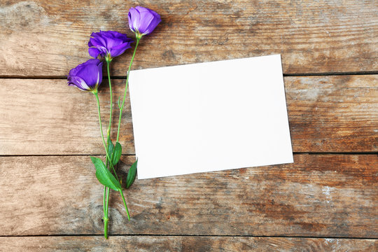 White sheet and violet blossom on wooden background, empty space