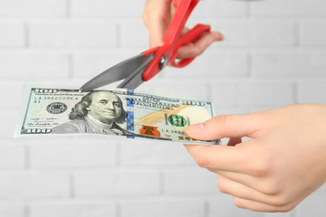 Hands with scissors cutting money on white brick wall background