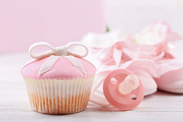 Obraz na płótnie Canvas Tasty cupcake with bow and baby shoes, decorative baby carriage on color background