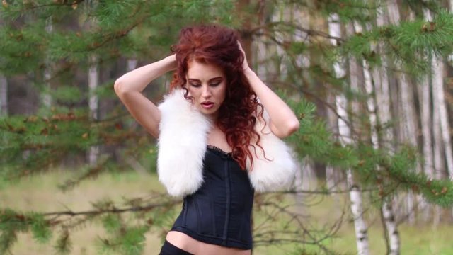 Pretty young woman poses with fur in autumn forest at sunny day
