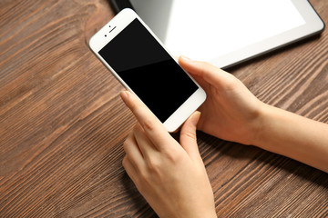 A tablet and female hands using mobile phone, on the wooden background