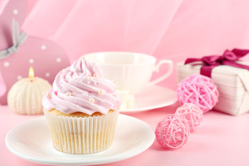 Tasty cupcake with gifts and decorations on pink background
