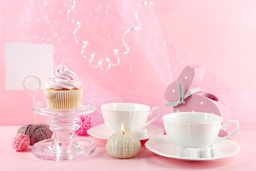 Tasty cupcake with tea set and decorations on pink background