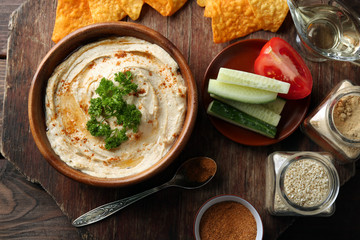 Wooden bowl of tasty hummus with chips, parsley on table