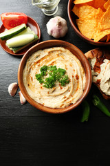 Wooden bowl of tasty hummus with chips and parsley on table