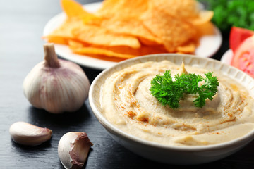 Ceramic bowl of tasty hummus with chips and parsley on table