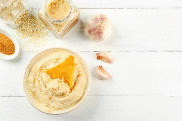 Ceramic bowl of tasty hummus with chips, spices and garlic on table