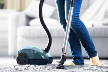 Woman cleaning the carpet with vacuum cleaner in the living room