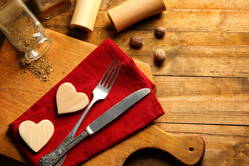 Fototapeta na wymiar Composition of fork, knife, napkin and decorative hearts on cutting board, on wooden table background