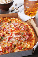 Tasty pizza in carton and glass of beer are on wooden table, close up