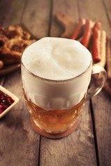 Glass of beer, chicken wings and grilled sausages on wooden table, close up