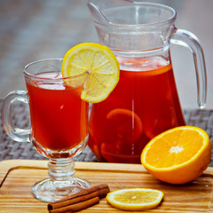 Refreshing summer fruit lemonade with orange and cinnamon in a beautiful glass and jar on wooden background