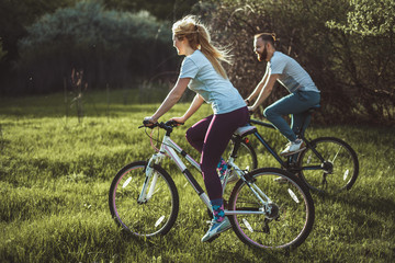 Fototapeta na wymiar Beautiful young girl and man walking with a bike ride on the green grass. The concept of active rest