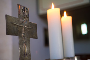 warmes Kerzenlicht im Altarraum mit Kreuz und zwei brennenden Kerzen