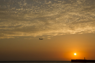 Airplane flying above sea at sunset