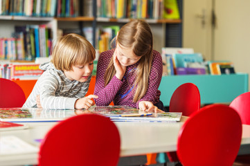 Two adorable kids, little girl and her brothe reading book in a library