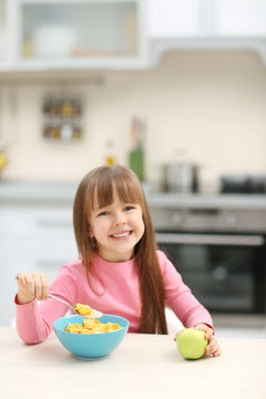 Beautiful little girl having breakfast with cereal and apple in kitchen