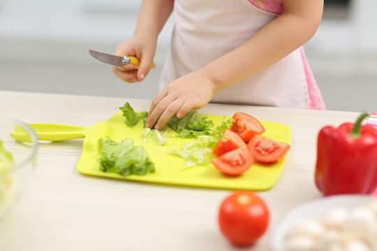 Little girl's  hands cutting vegetables on a board.