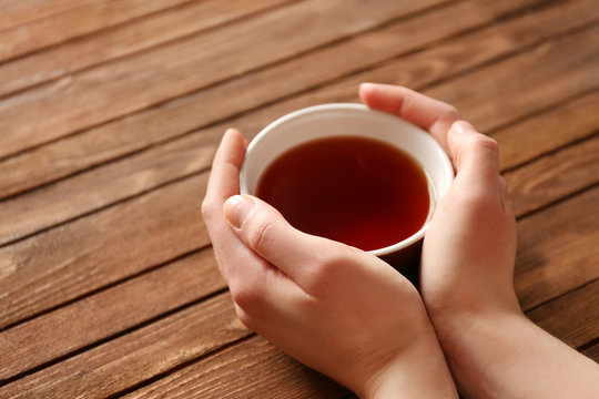 Female hands holding cup of tea on wooden background