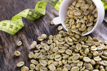 Green coffee beans in a white cup with measuring tape on wooden table