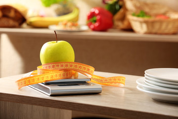 Apple with centimeter and digital kitchen scales on wooden table
