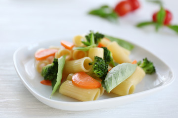 Boiled rigatoni pasta with carrot, broccoli and basil on white plate