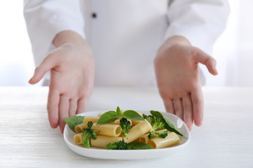 Female chef holding plate of boiled rigatoni pasta with broccoli and basil at the table