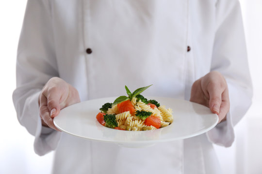 Female chef holding plate of boiled fusilli pasta with salmon and broccoli