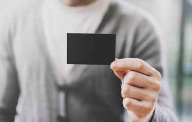 Man wearing casual shirt and showing empty black business card. Blurred background. Ready for private information. Horizontal mockup